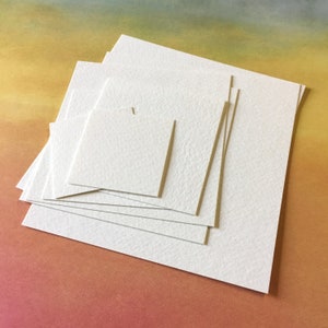 Pode incluir: Uma pilha de quadrados de papel branco texturizado, perfeitos para pintura em aquarela ou outros projetos de arte.