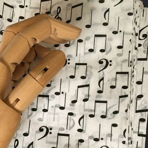 May include: A stack of white tissue paper with a black musical note pattern. The tissue paper is being held by a wooden hand.