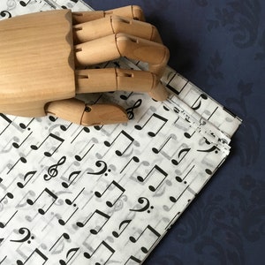 May include: A wooden hand model resting on a sheet of white paper with black musical notes printed on it. The paper is folded over on itself.