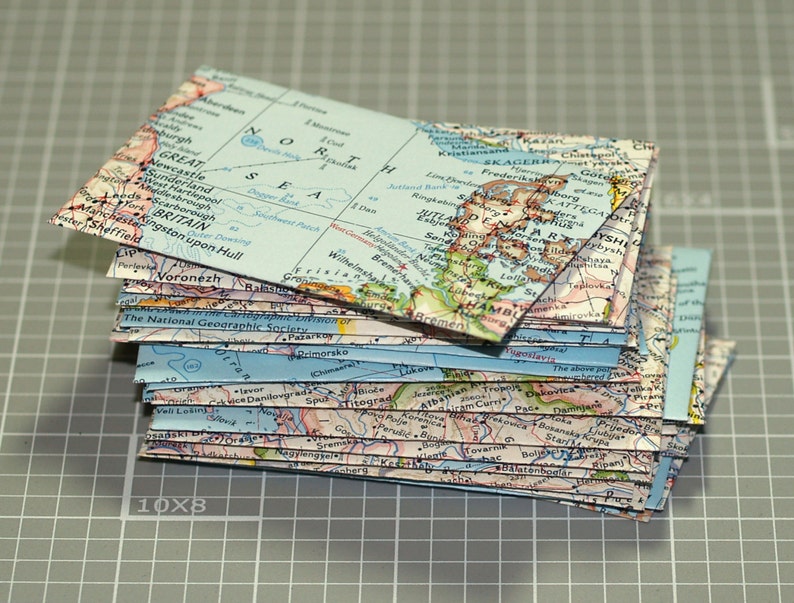 May include: A stack of vintage map postcards, featuring a variety of locations, including Great Britain, Scandinavia, and Russia. The postcards are in various shades of blue, green, and brown, with white text and borders.
