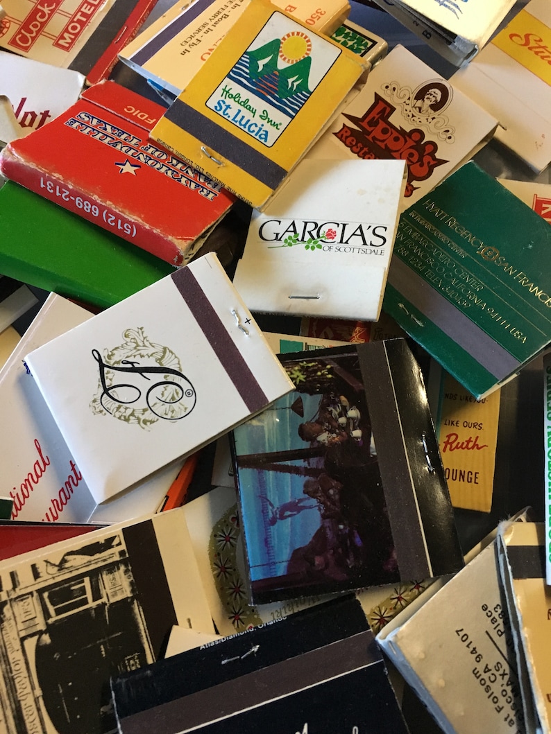 May include: A collection of vintage matchbooks with various designs and text. Some of the matchbooks feature images of hotels, restaurants, and businesses. The matchbooks are in various colors, including red, green, yellow, and blue.