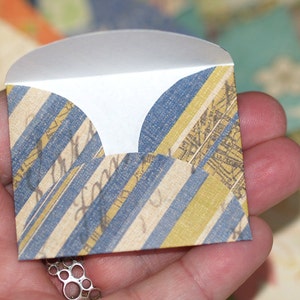 May include: A small, folded envelope with a blue and yellow striped pattern. The envelope has a scalloped edge and is made of paper.