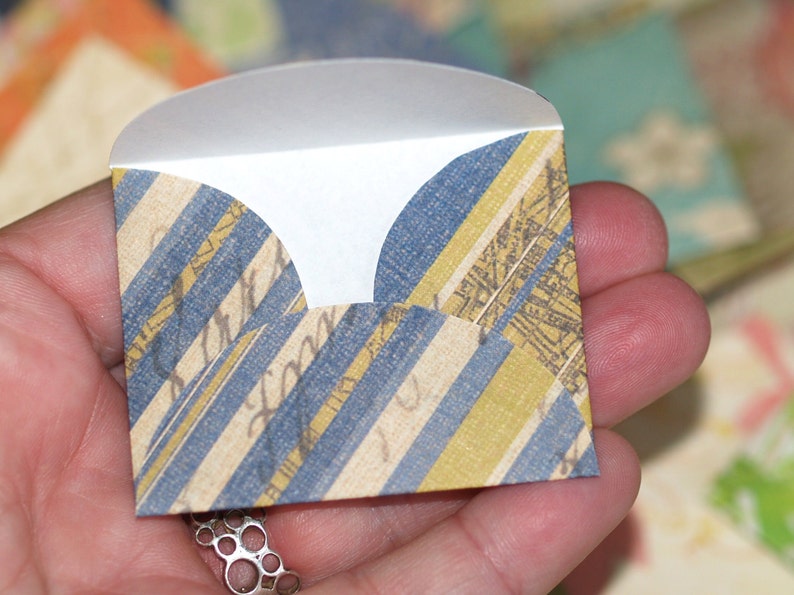 May include: A small, folded envelope with a blue and yellow striped pattern. The envelope has a scalloped edge and is made of paper.