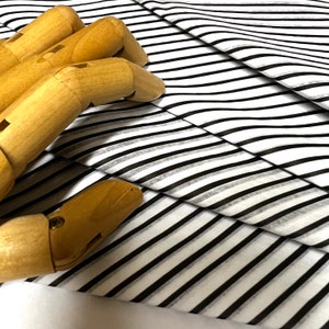 May include: A white and black striped fabric with a wooden hand model on top. The fabric is folded over itself, creating a layered effect.