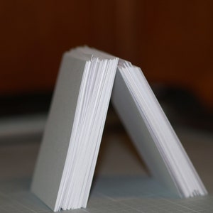 May include: A stack of white paper cards fanned out to form a triangular shape.