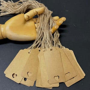 May include: A set of brown kraft paper gift tags with a heart-shaped cut-out. The tags are tied together with twine and are ready to be used for gift wrapping.