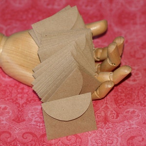 May include: A stack of brown paper envelopes with a rounded flap. The envelopes are held in a wooden hand.