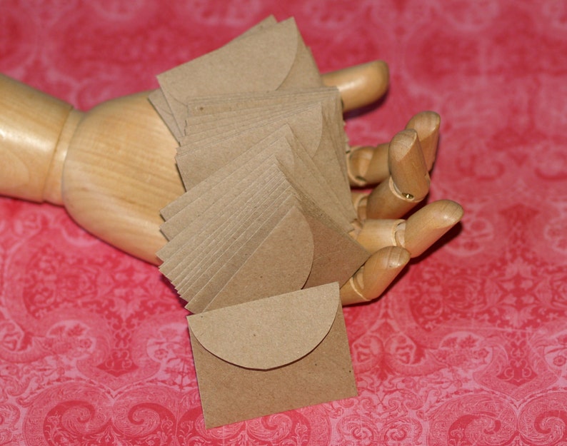 May include: A stack of brown paper envelopes with a rounded flap. The envelopes are held in a wooden hand.