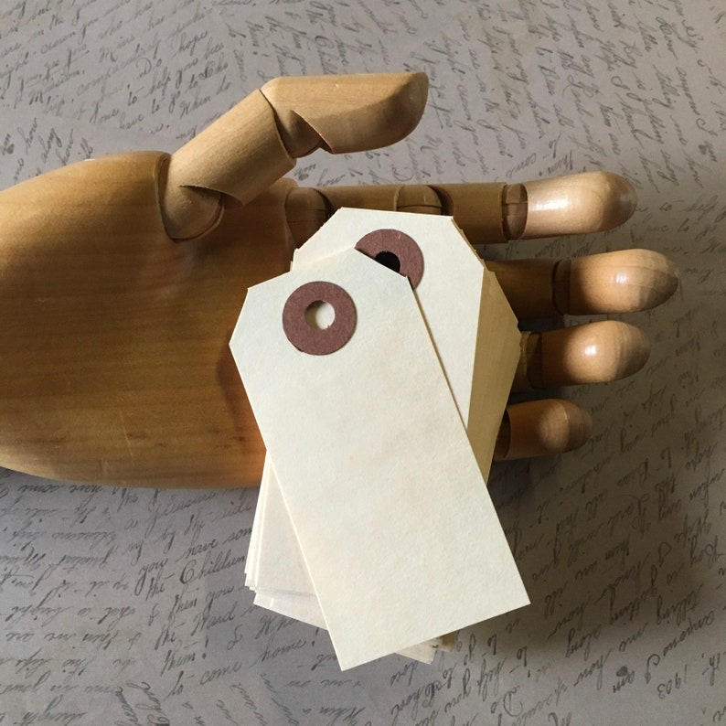 Op de afbeelding: Een stapel blanco, cr&egrave;mekleurige cadeau-etiketten met bruine oogjes. De etiketten zijn gerangschikt in een handvormige houten display.
