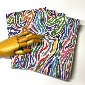May include: Multicolored fabric with a zebra stripe pattern in shades of blue, green, red, yellow, and purple. The fabric is folded and has a white background.