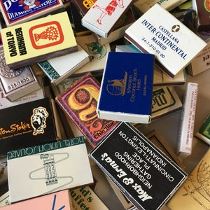 May include: A pile of matchboxes with various designs and logos. Some of the matchboxes feature hotel names, such as "Sheraton Coconut Beach Hotel" and "Hotel Union Square". Other matchboxes feature company logos, such as "Domino Diamond Matches" and "Benihana of Tokyo".