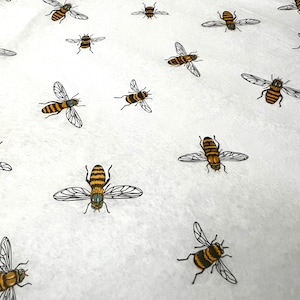 May include: White fabric with a repeating pattern of yellow and black bees. The bees are stylized and have a cartoonish appearance.