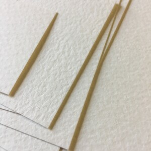 Pode incluir: Uma pilha de papel branco texturizado com finas tiras de papel castanho no topo.