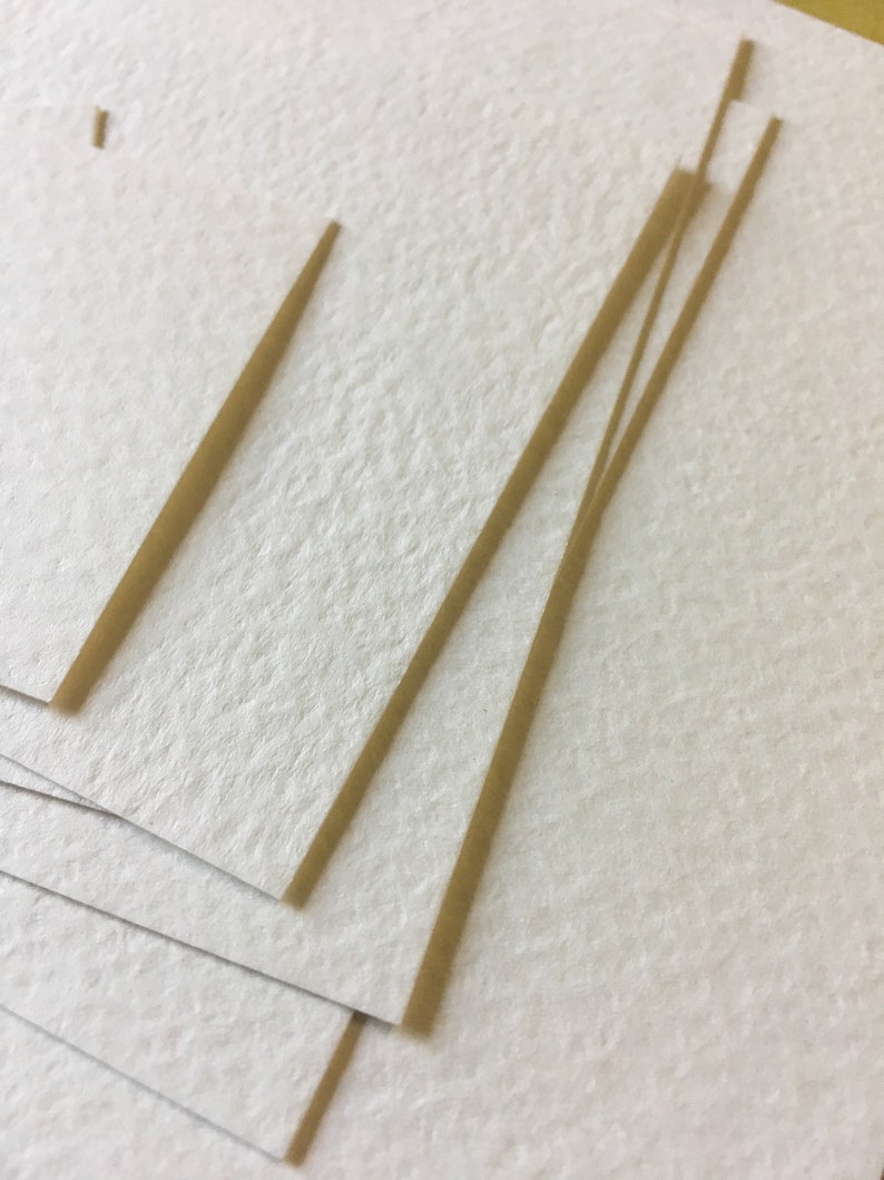Pode incluir: Uma pilha de papel branco texturizado com finas tiras de papel castanho no topo.