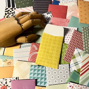May include: A collection of colorful patterned envelopes with a wooden hand holding a yellow envelope with a geometric pattern. The envelopes are perfect for sending letters, notes, or invitations.