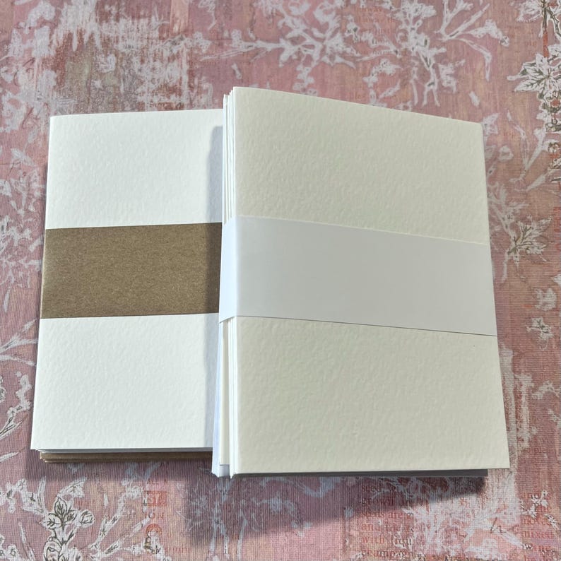 May include: Two stacks of blank white note cards with brown paper backing. The cards have a textured surface.