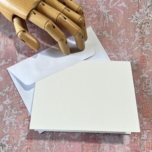 May include: A blank white card with a white envelope. The card is slightly larger than the envelope.