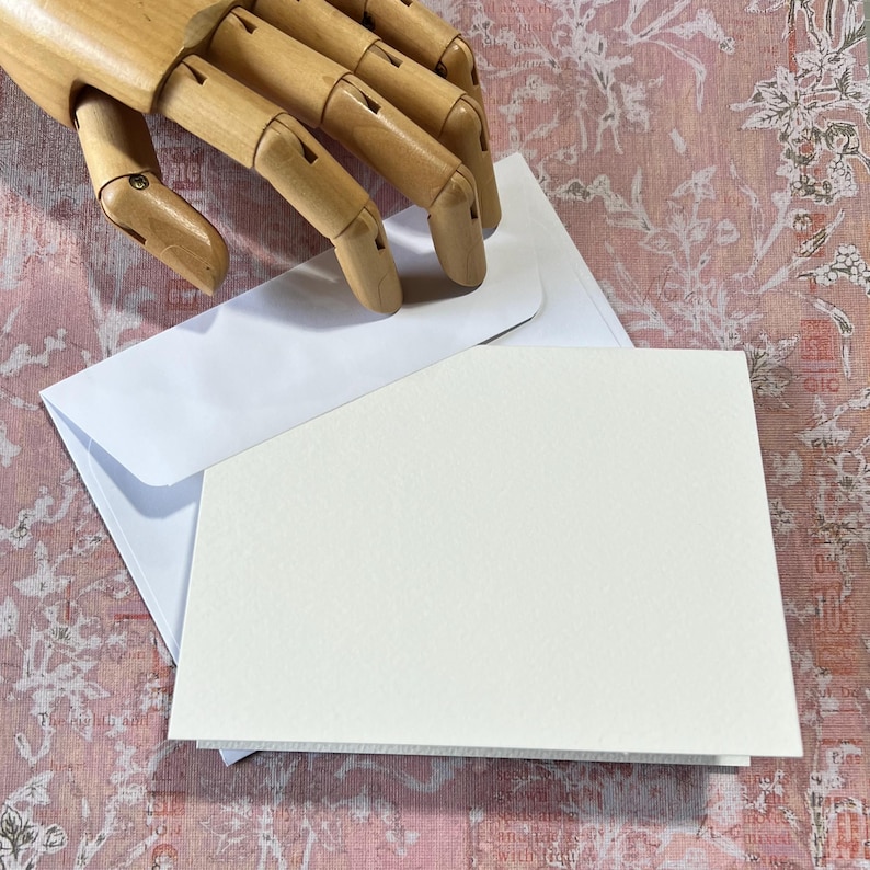 May include: A blank white card with a white envelope. The card is slightly larger than the envelope.