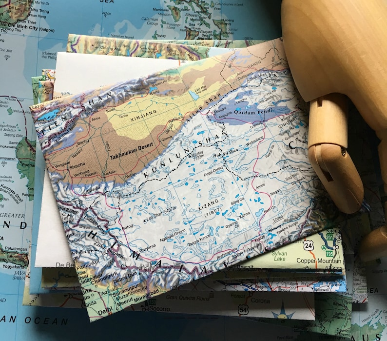 May include: A close-up of a map of Asia, showing the Taklimakan Desert, the Kunlun Mountains, and the Tibetan Plateau. The map is printed on a white background with blue and red lines.