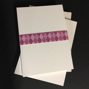 May include: A stack of three white cardstock sheets with a pink and white diamond patterned ribbon around the middle sheet.