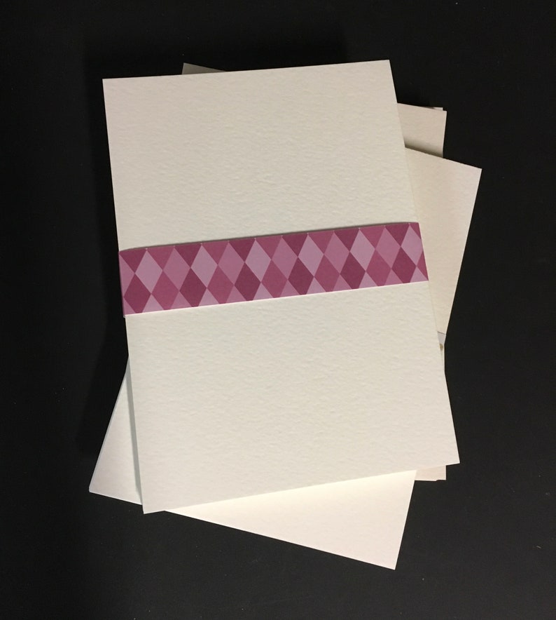 May include: A stack of three white cardstock sheets with a pink and white diamond patterned ribbon around the middle sheet.
