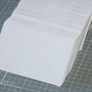 May include: A stack of white blank cards on a gray grid surface.