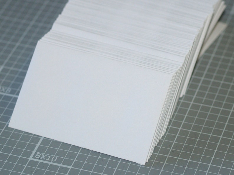 May include: A stack of white blank cards on a gray grid surface.