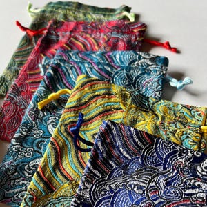 May include: A stack of colorful drawstring pouches with intricate patterns. The pouches are made of a silky fabric and have a variety of colors, including red, blue, green, and yellow.