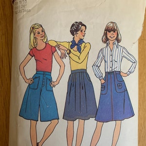 May include: A vintage Simplicity sewing pattern for girls' skirts, sizes 9-10, with a waist measurement of 24 inches. The pattern features three different skirt styles: a blue cuffed skirt with pockets, a blue A-line skirt, and a yellow A-line skirt with a contrasting neckline.