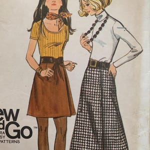 Puede incluir: Patrón de costura vintage con dos mujeres que llevan faldas. La mujer de la izquierda lleva una blusa amarilla con una falda marrón y un cinturón marrón. La mujer de la derecha lleva un jersey blanco de cuello alto con una falda a cuadros blanco y negro y un cinturón marrón. El patrón se titula "Sew & Go" y tiene el número 23 1/2.