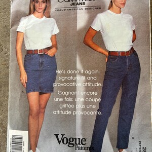 May include: A vintage Vogue Patterns sewing pattern featuring Calvin Klein Jeans. The pattern shows two models wearing denim jeans and a denim skirt with white t-shirts and brown belts. The text reads "He's done it again: signature fit and provocative attitude."