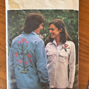 May include: A vintage sewing pattern from Butterick, The Fashion One, featuring a couple wearing embroidered shirts. The pattern number is 4741 and the price is $1.50. The woman's shirt has a red bird embroidered on the pocket, and the man's shirt has a tree with pink flowers embroidered on the back.