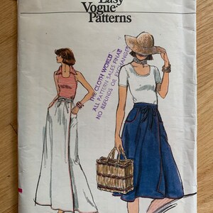 May include: Vintage sewing pattern for a wrap skirt, featuring two models wearing different styles of the skirt. The pattern is from Very Easy Vogue Patterns and is size 26 1/2. The text "THE CLOTH WORLD ALL PATTERN SALES FINAL NO REFUNDS OR EXCHANGE" is printed on the pattern.