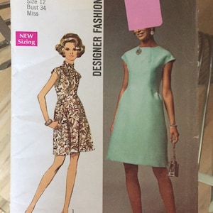May include: A vintage Simplicity sewing pattern for a dress, featuring two different styles. The pattern number is 8534 and the price is £1.00. The pattern is for a size 12, bust 34, miss. The dress on the left is a brown and white floral print, while the dress on the right is a solid light blue.