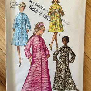May include: A vintage Simplicity sewing pattern for a long robe with three different styles. The pattern is for sizes 14 and bust 36. The pattern shows three different styles of robes: a light blue robe with lace trim, a pink robe with a grid pattern, and a leopard print robe. The pattern is titled "House of Fabrics" and has the number 9074.