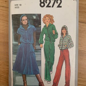Puede incluir: Patrón de costura Simplicity 8272 con ilustraciones de chándales con capucha y un traje de falda. El patrón incluye una talla 10 Miss. La portada muestra a mujeres con varios atuendos, incluyendo un traje de falda azul y chándales verdes y rojos.