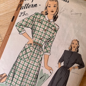 Puede incluir: Patrón de costura vintage para un vestido, con un patrón a cuadros y un vestido negro sólido. El patrón está etiquetado como "Hollywood Pattern" y tiene el número 1665 impreso.
