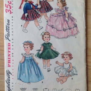 May include: A vintage Simplicity sewing pattern for doll clothes. The pattern is for a 23-inch doll and includes five different dress designs. The pattern is printed on a white paper with a pink and blue border. The pattern is titled "Simplicity Printed Pattern" and has the number 35c on it.