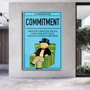 Puede incluir: Un póster enmarcado con un fondo azul claro con la palabra "COMMITMENT" en letras negras en negrita. La imagen incluye una caricatura de un hombre con traje sentado en un trono hecho de dinero. El texto dice "BY BEING HERE TO STAY, SPECIAL ISSUE."