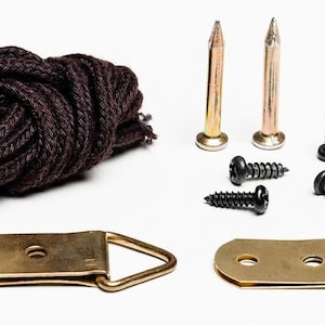 May include: A selection of picture hanging hardware, featuring two brass-coloured D-rings, a bundle of dark brown rope, two gold-coloured nails, and four black screws. The items are arranged on a white background.
