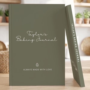 Puede incluir: Un diario de tapa dura color verde salvia con el texto Taylor's Baking Journal en letra cursiva blanca, un pequeño icono de cupcake y el texto ALWAYS MADE WITH LOVE. El lomo también muestra el texto TAYLOR'S BAKING JOURNAL en mayúsculas.