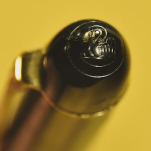 Op de afbeelding: Een witte keramische mok met een zwarte handgreep en de tekst "But First, Coffee" in een vetgedrukte, zwarte letter. De mok staat tegen een vage achtergrond, wat een gezellige setting suggereert.