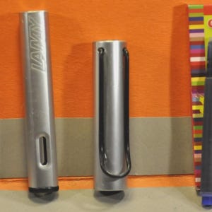 K&ouml;nnte beinhalten: Ein silberner Lamy-F&uuml;llhalter, zerlegt in Federteil, Schaft und Kappe, neben einer blauen Tintenpatrone und einer Schachtel Herlitz Universal-Patronen mit dem Text Standard, Lamy und K&ouml;nigsblau.
