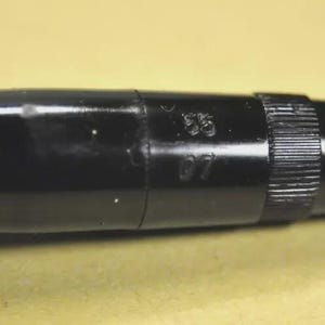 Puede incluir: Un cuerpo de bol&iacute;grafo cil&iacute;ndrico de color negro brillante con una secci&oacute;n de agarre texturizada cerca del extremo. La superficie est&aacute; marcada con los n&uacute;meros 55 y 07 en relieve, claramente visibles en el lateral de la carcasa de pl&aacute;stico negro.