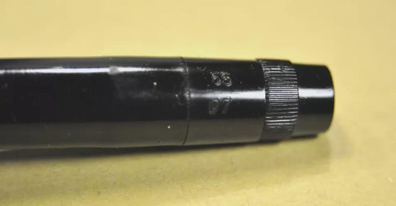 Puede incluir: Un cuerpo de bol&iacute;grafo cil&iacute;ndrico de color negro brillante con una secci&oacute;n de agarre texturizada cerca del extremo. La superficie est&aacute; marcada con los n&uacute;meros 55 y 07 en relieve, claramente visibles en el lateral de la carcasa de pl&aacute;stico negro.