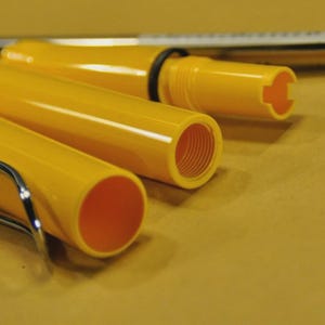 Puede incluir: Un bol&iacute;grafo amarillo desmontado con un clip plateado y un bol&iacute;grafo de tinta negra con una tapa azul. Las piezas del bol&iacute;grafo est&aacute;n dispuestas sobre una superficie amarilla, mostrando los componentes internos del instrumento de escritura. El dise&ntilde;o del bol&iacute;grafo es simple y funcional.