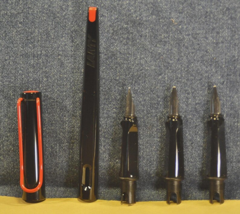 K&ouml;nnte beinhalten: Schwarzer F&uuml;llfederhalter mit roten Akzenten, einschlie&szlig;lich Kappe und Clip. Der Stiftk&ouml;rper ist schwarz und der Clip rot. Das Bild zeigt auch die Federn des Stifts und andere Komponenten.