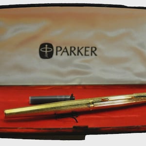 Peut inclure: Un stylo plume Parker doré et une cartouche d'encre noire, présenté dans un coffret noir ouvert avec un intérieur rouge. Le couvercle de la boîte porte le logo et le nom de la marque Parker en noir.