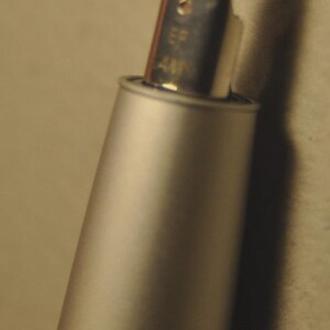 May include: Close-up of a silver fountain pen nib with the text "EF 4M" visible. The pen's body is a matte silver color, and the nib is highly polished, reflecting light. The pen is angled, with a soft background.