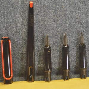 K&ouml;nnte beinhalten: Ein schwarzer Lamy-Stift mit roter Akzentfarbe auf der Kappe und einer roten Spitze. Der Stift ist zerlegt und zeigt die Federn und den Stiftk&ouml;rper. Das Lamy-Logo ist auf dem Stiftk&ouml;rper sichtbar.